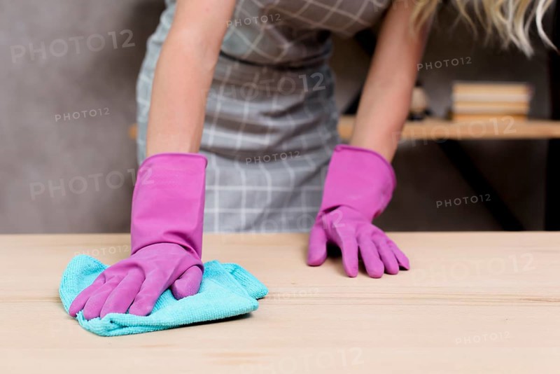 Midsection female janitor wiping wooden table with cloth