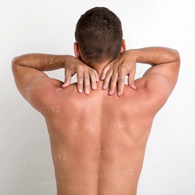 Rear view shirtless man having back pain standing against white wall