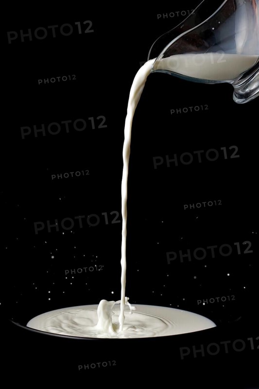 Pitcher with milk pouring on a plate with splash effect on a black background