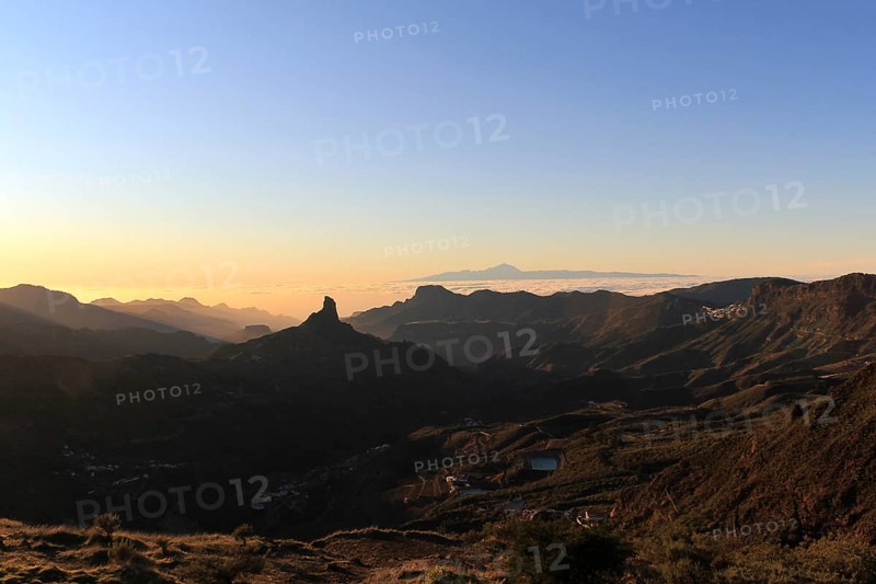 View of Roque Nublo on Gran Canaria with the silhouete of the Teide mountain in the background and a sea cloud. Sunset in Gran Canaria. Roque Nublo and El Teide together