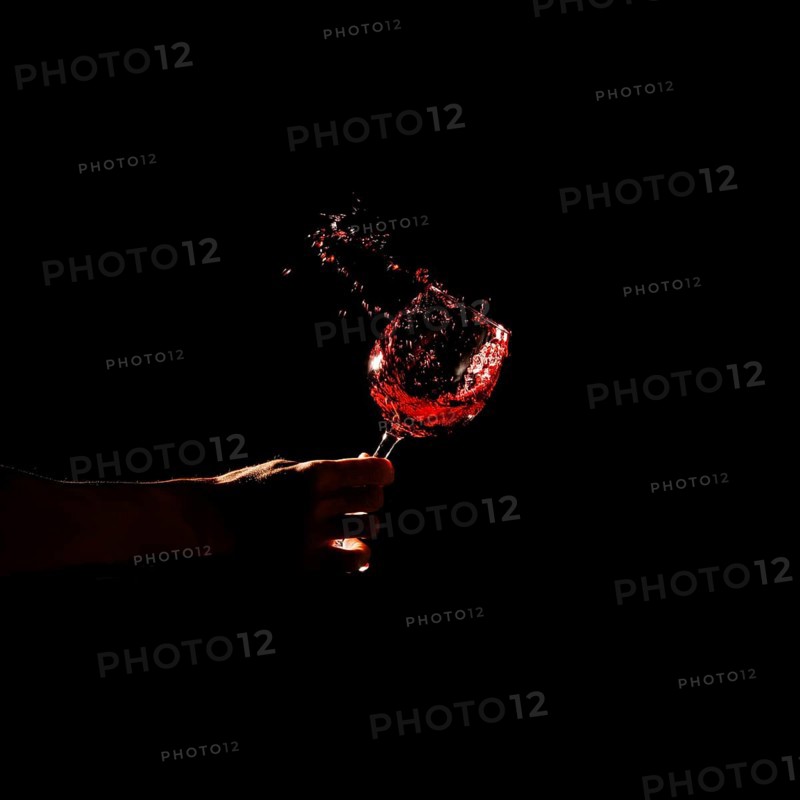 Person s hand holding glass red wine splashing out glass