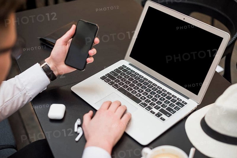 Young businessman using laptop looking smartphone screen