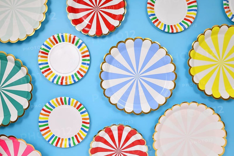 Different colorful striped paper party plates on blue background