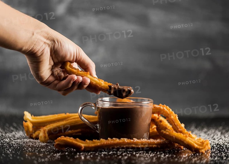 Hand dipping fried churros chocolate front view
