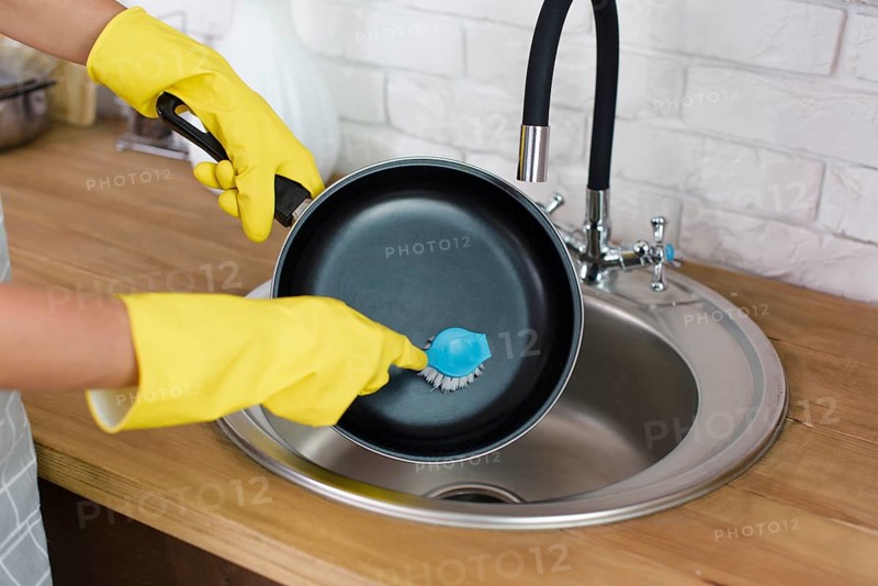 Person hand with yellow glove washing pan with brush kitchen