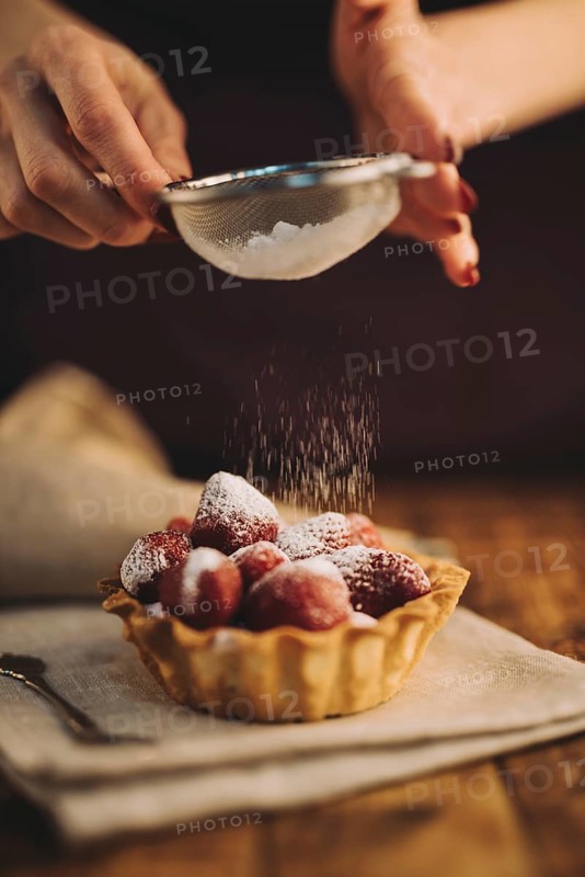 Woman dusting sugar powder strawberry tart