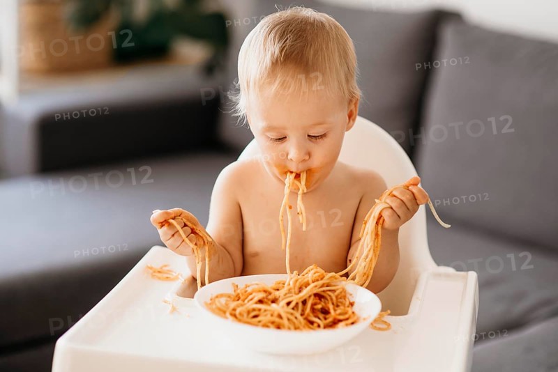 Front view baby boy playing with pasta his highchair