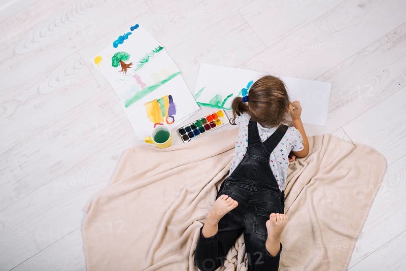 Girl painting by water colors paper lying floor