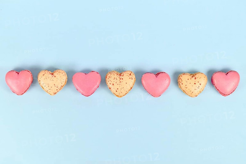 Pink and yellow heart shaped French macaron sweets in a row on blue background