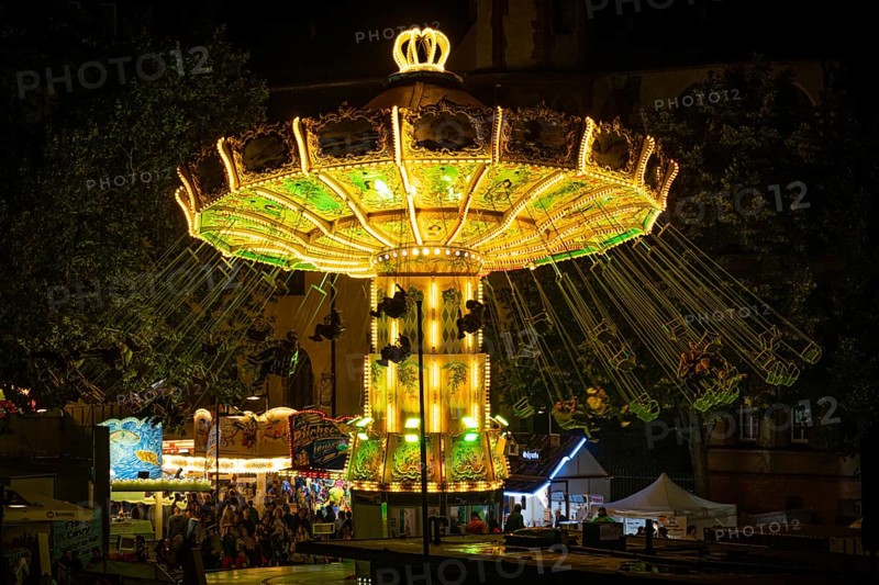 The colourful lights of the carousel at the Mainfest glow in the evening. The Mainfest on the Mainkai