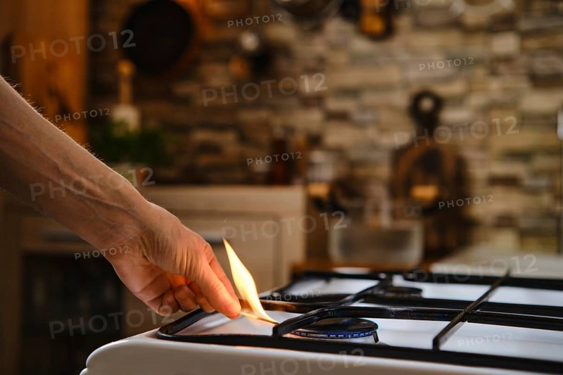 Unrecognizable man lights gas on the stove with match