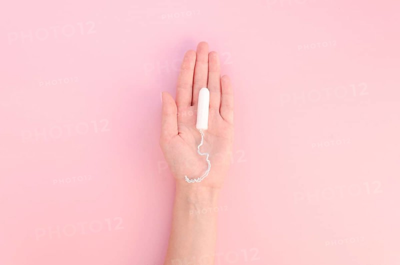 Hand holding tampon pink background