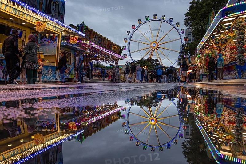 The colourful lights of the Mainfest are reflected in a puddle. The Mainfest on the Mainkai