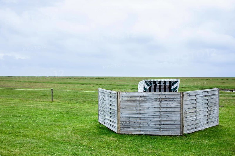 Beach chair in a meadow on the Wadden Sea with windbreak in front of it