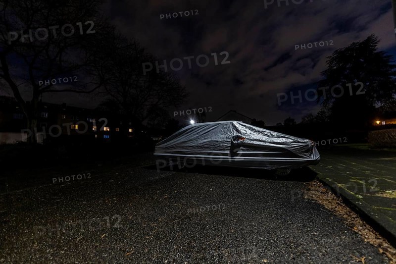 Covered car parked on the street under a lamppost at night