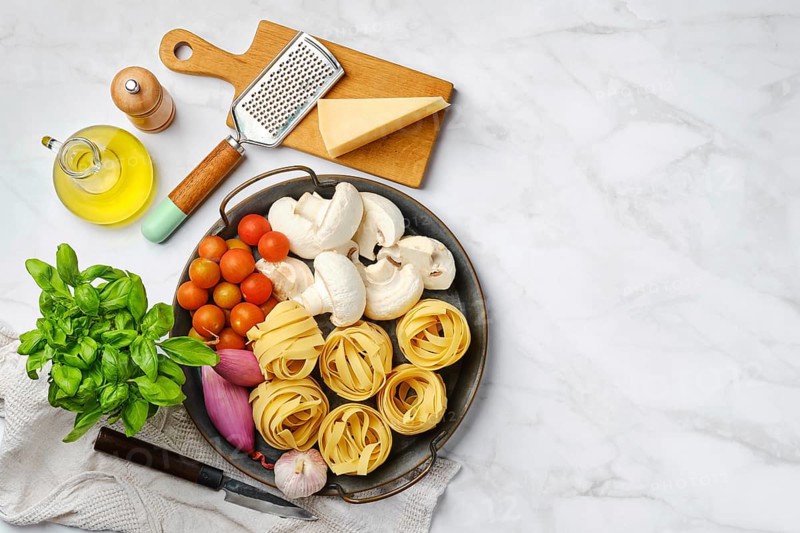Top view of raw ingredients for mushroom pasta on marble background