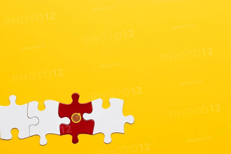 Red jigsaw puzzle piece with dartboard symbol arranged with white piece yellow background