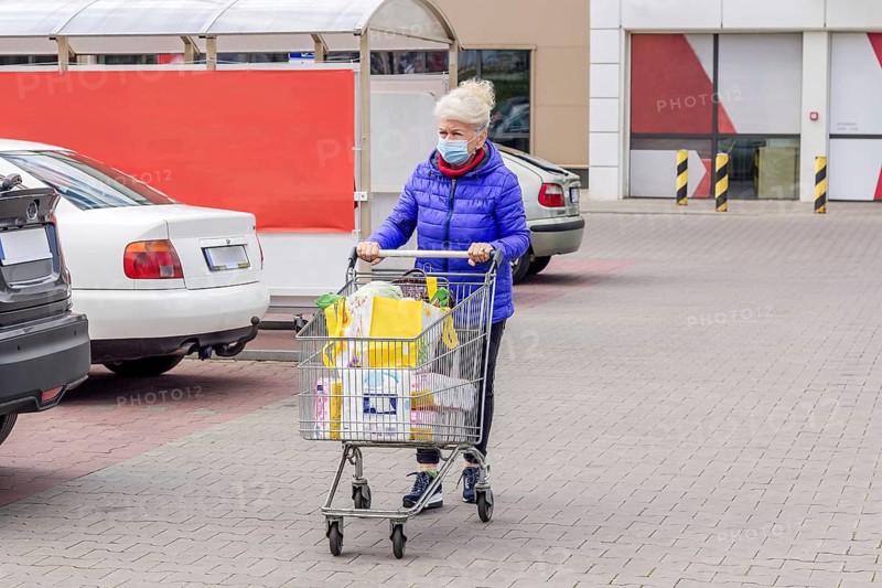Shot of mature woman wearing protective mask with shopping cart on the parking lot during coronavirus pandemic. Everyday life