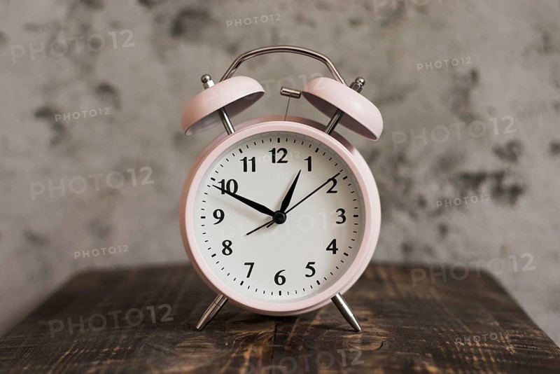 Pink alarm clock wooden desk against weathered wall