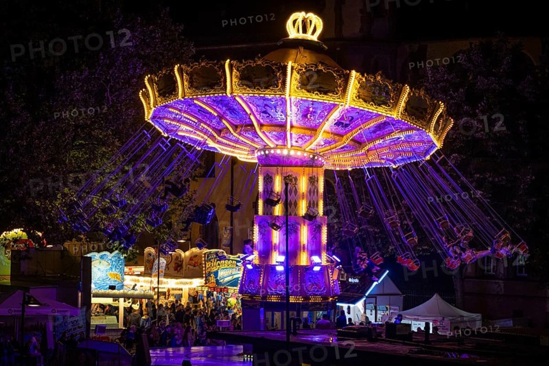 The colourful lights of the carousel at the Mainfest glow in the evening. The Mainfest on the Mainkai