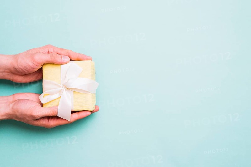 Person s hand holding small gift box against blue background