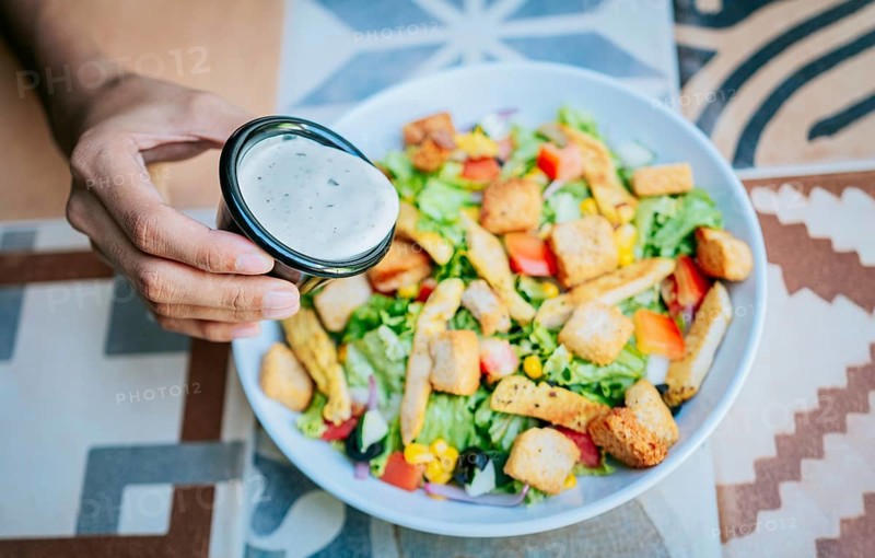 Concept of healthy food and lifestyle. Hand putting dressing on a caesar salad