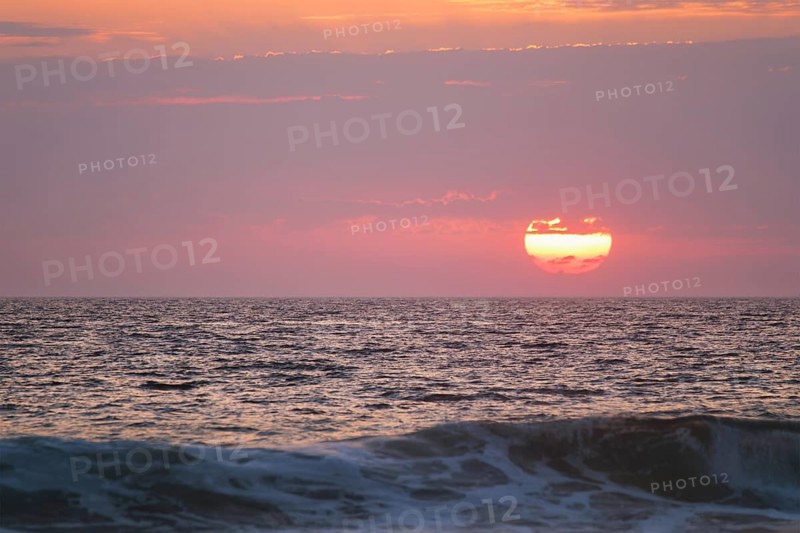 Ocean waves on sunset with setting sun background