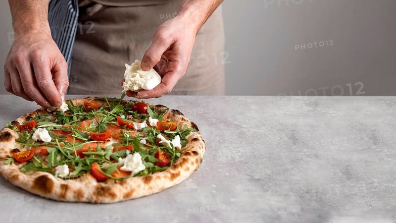 Man putting mozzarella baked pizza dough with smoked salmon slices