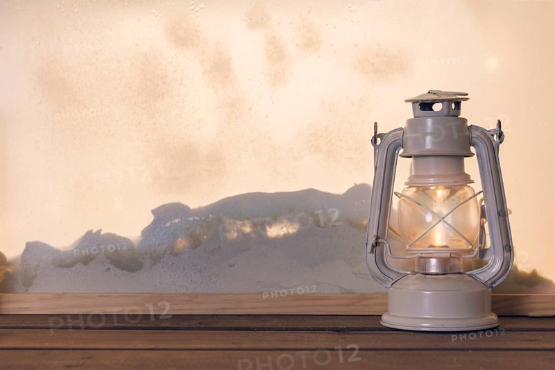Gas lantern wooden board near heap snow through window