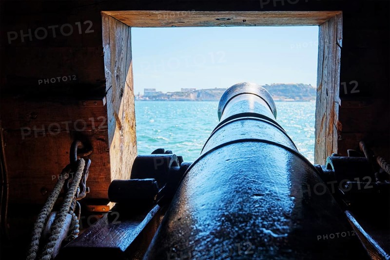 Sea view out of a gunport in hull of the ship over the gun cannon muzzle in on the gun deck of a sailing ship of Age of Sail