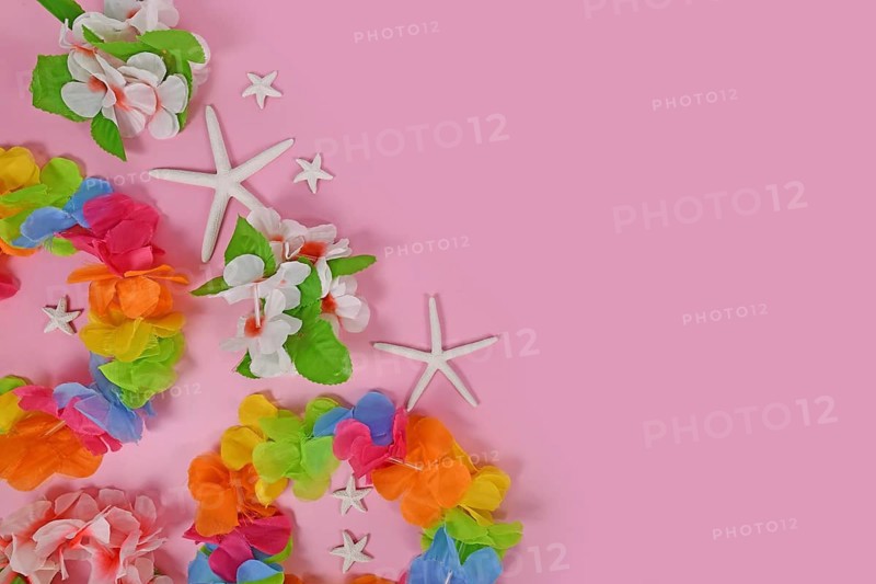 Bright flower lei necklaces on side of pink background with copy space