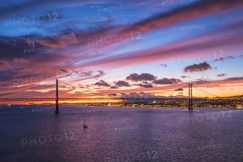 View of 25 de Abril Bridge famous tourist landmark of Lisbon connecting Lisboa and Almada on Setubal Peninsula over Tagus river in the evening twilight with boats. Lisbon