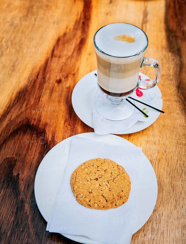 Close up of cookie and cappuccino on wooden table. Top view glass of hot cappuccino with cookie on wooden background