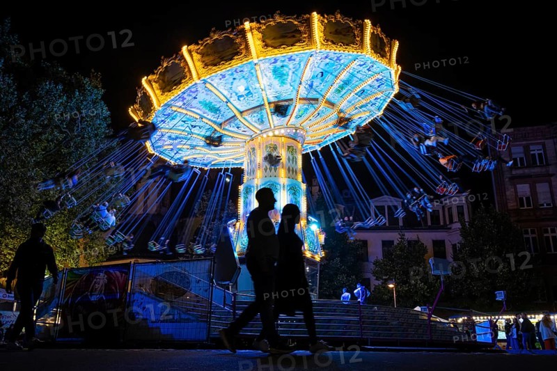 The colourful lights of the carousel at the Mainfest glow in the evening. The Mainfest on the Mainkai