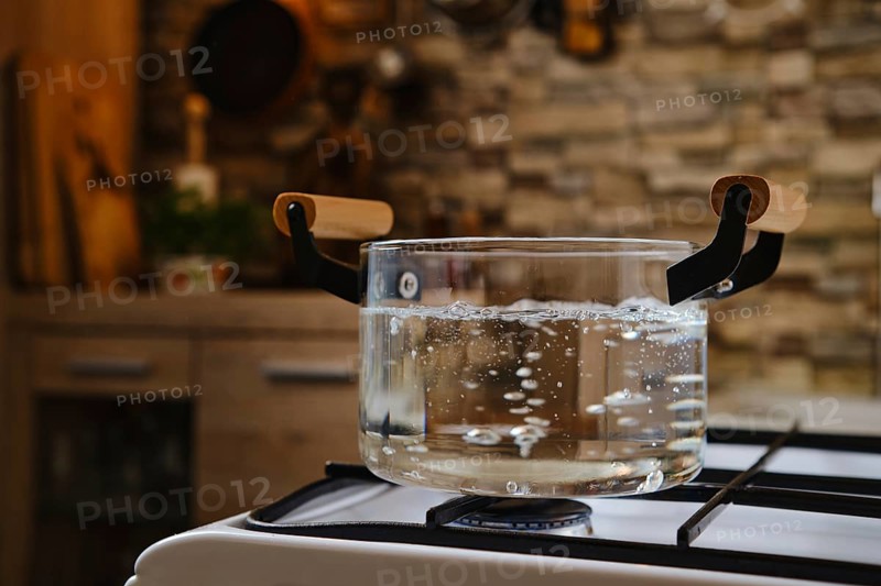 Water boiling in transparent glass pot on stove