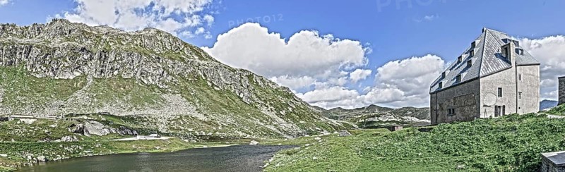 Photo with reduced dynamics saturation HDR of view on left mountain lake right historical hotel accommodation Ospizio San Gottardo Sankt Gotthard Hospice with historical building fabric from year 1237 13th century on 2091 metres high Gotthard Pass