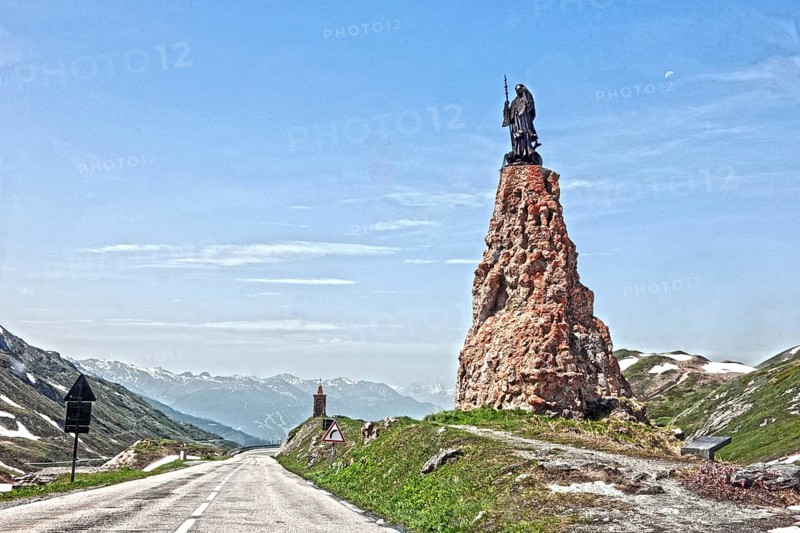 Photo with reduced dynamic saturation HDR of mountain pass alpine mountain road alpine road pass road pass above tree line with right monument with statue of Saint Bernard of Menthon on top of Little Saint Bernard Pass