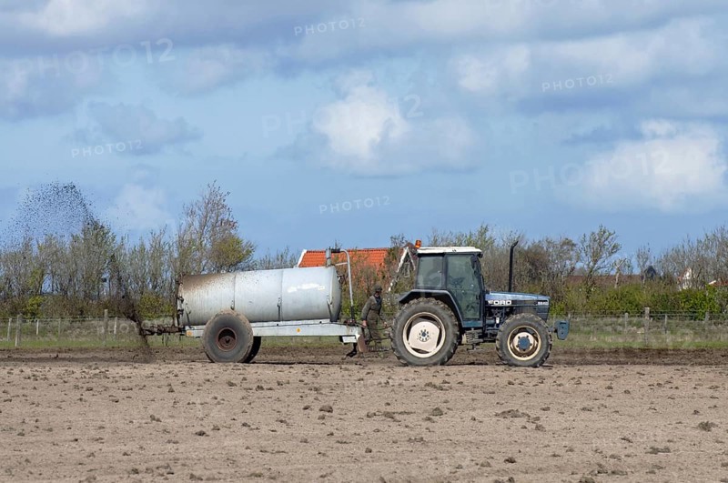 Tractor spreading manure to fertilize field