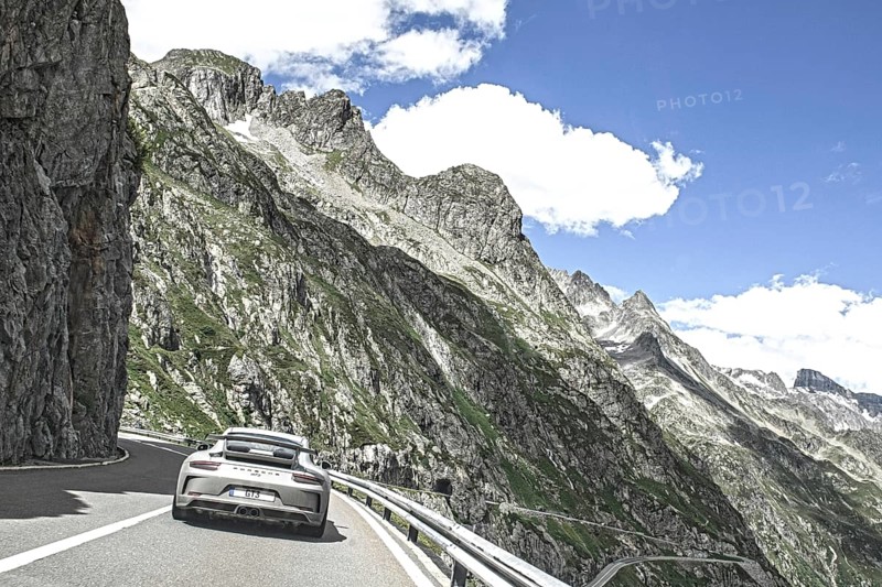 Photo with reduced dynamic range saturation HDR of view of Porsche 911 GT3 driving on mountain road above tree line Alpine pass Mountain pass in high Alps