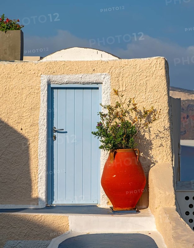 Red vase in front of yellow wall with blue door