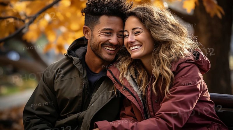 Happy warmly dressed young loving multi-ethnic couple laughing as they enjoy the beautiful fall leaves in the park