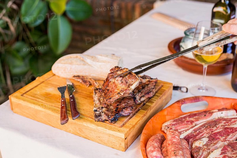 Person holding fresh grilled beef steak with tong wooden board