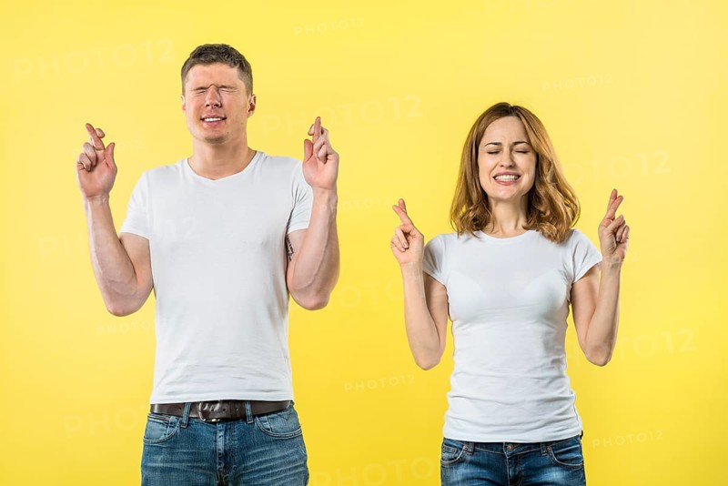 Smiling young couple crosses fingers anticipation something pleasant