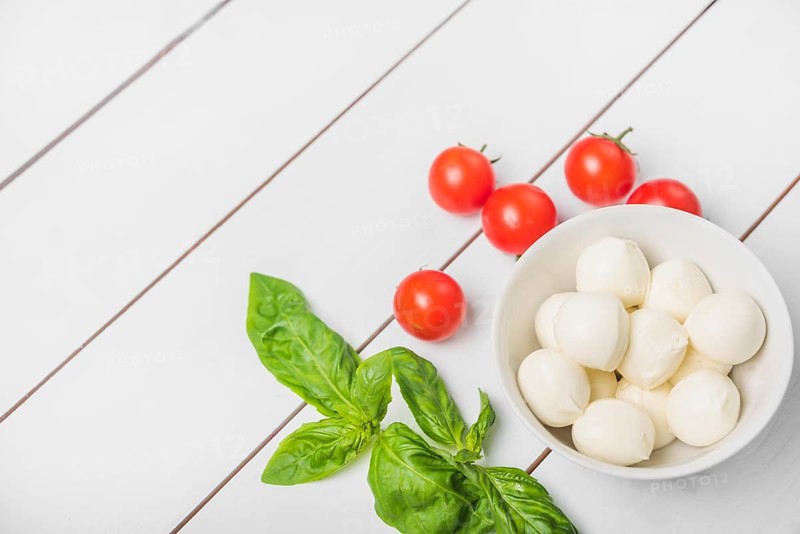 Mozzarella cheese ball with basil leaf red tomatoes wooden white background