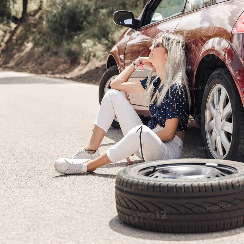 Sad young woman sitting near broken down car road