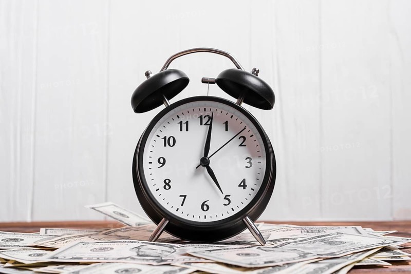 Alarm clock us dollar currency notes wooden desk against white wall
