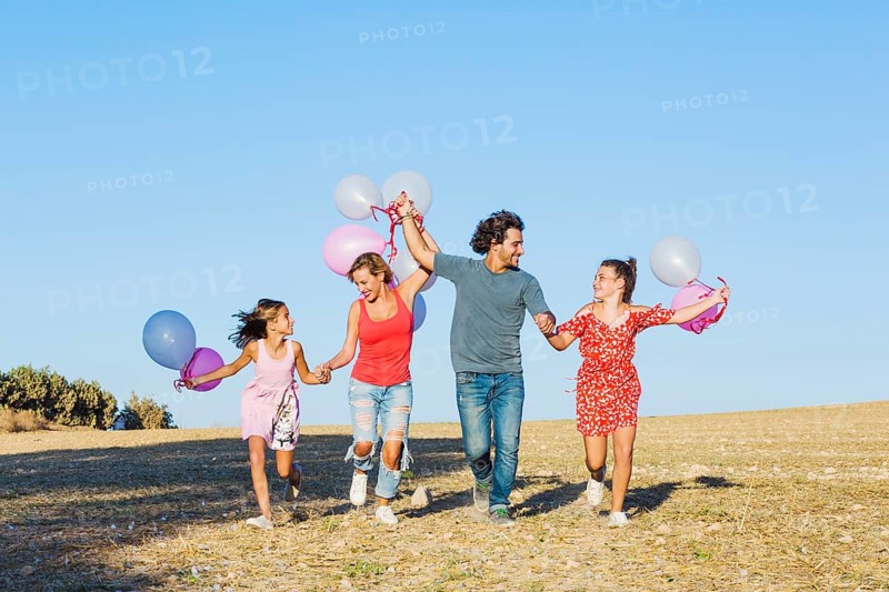 Family running field holding balloons