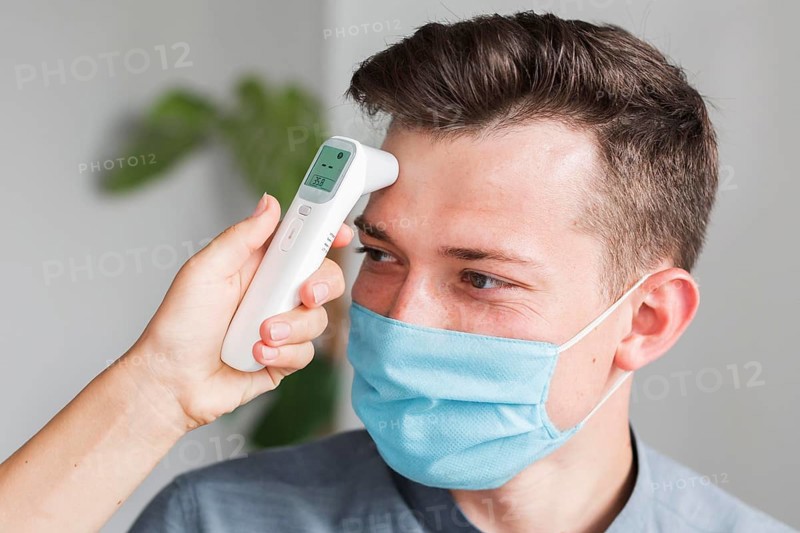 Man with medical mask checking temperature office with thermometer