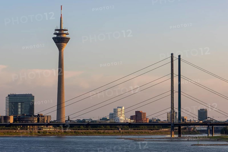 Rheinturm and Rheinkniebruecke illuminated by the setting sun and behind them Neuer Zollhof and Gehry buildings