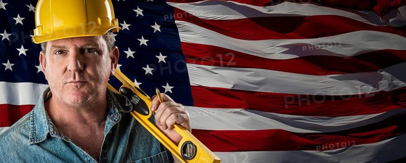 Male contractor wearing blank yellow hardhat over waving american flag background banner